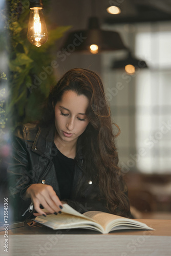 Mulher atrás do vidro de uma cafeteria lendo um livro