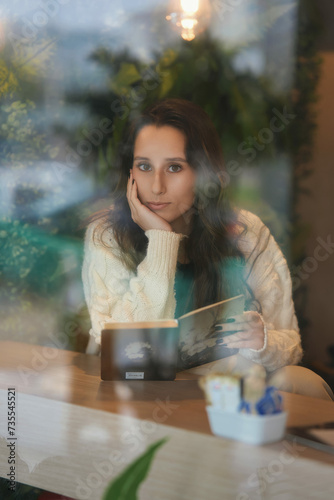 Mulher atrás do vidro de uma cafeteria lendo um livro