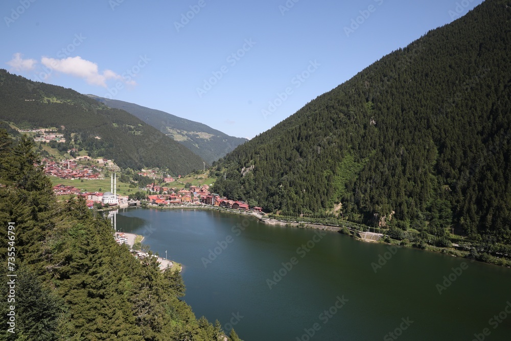 Buildings under mountains near lake on sunny day