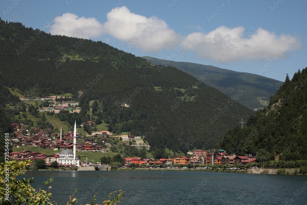 Buildings under mountains near lake on sunny day