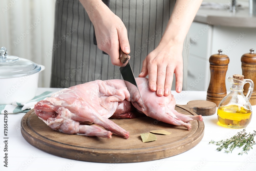 Woman cutting whole raw rabbit at white wooden table, closeup