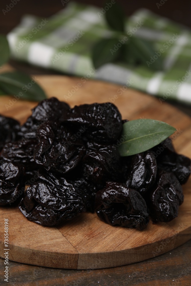 Tasty dried prunes and green leaf on wooden table, closeup Tasty dried prunes and green leaf on wooden table, closeup