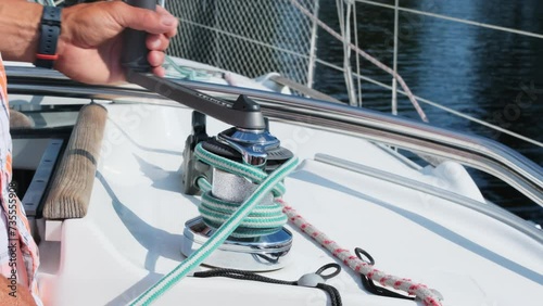 Seasoned yachtsman uses manual winch wrapping rope. Experienced skipper controls tension preparing lines before sailing in sea photo