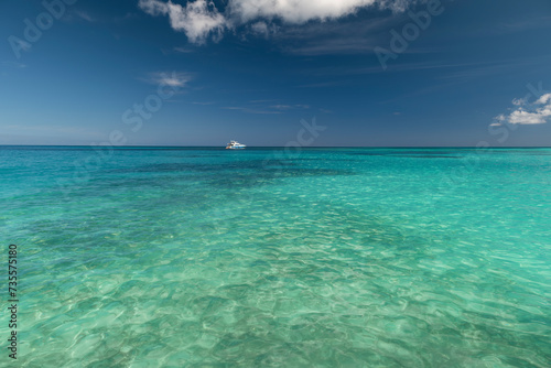 Seascape with crystal clear shallow turquoise water, deep blue sky and white yacht on the horizon. Saona Island, Dominican Republic. Wide angle shot.