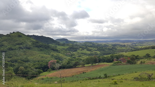 Paisagem com montanhas verdes, área de terra preparada para plantação, e céu carregado de nuvens escuras © Jorge F. Filho