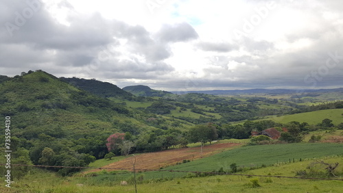 Paisagem com montanhas verdes, área de terra preparada para plantação, e céu carregado de nuvens escuras