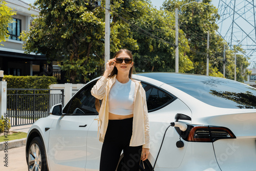 Eco-friendly conscious woman recharging EV vehicle from home charging station. EV electric car technology utilized as alternative transportation for future sustainability. Expedient photo