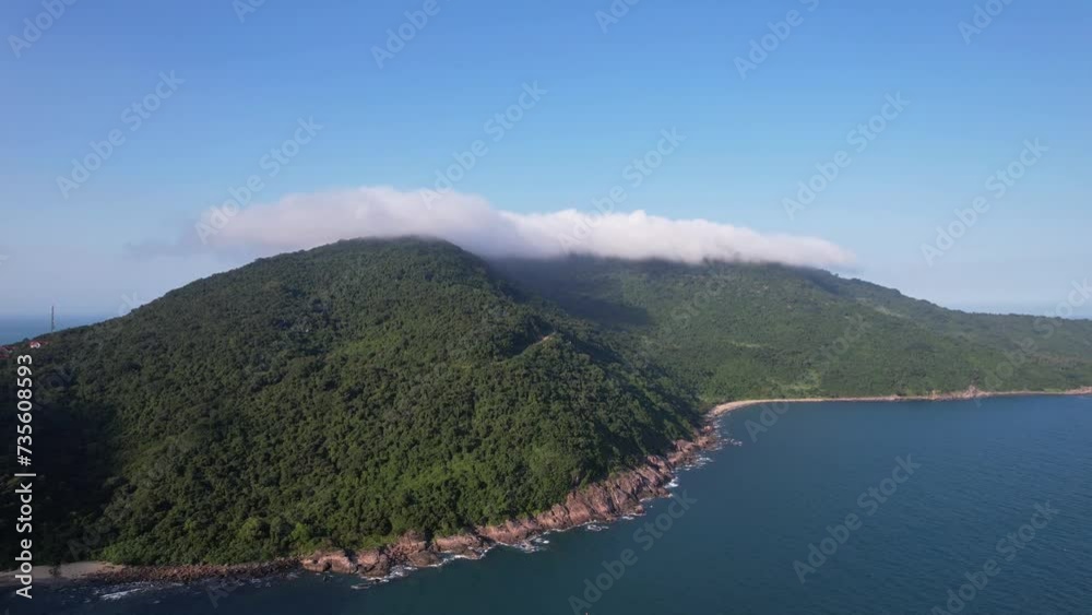 Aerial view of a lush green mountain with a cloud cap adjacent to a serene coastline, exemplifying untouched natural beauty and tranquility Aerial view of a lush green mountain with a cloud cap adjacent to a serene coastline, exemplifying untouched natural beauty and tranquility