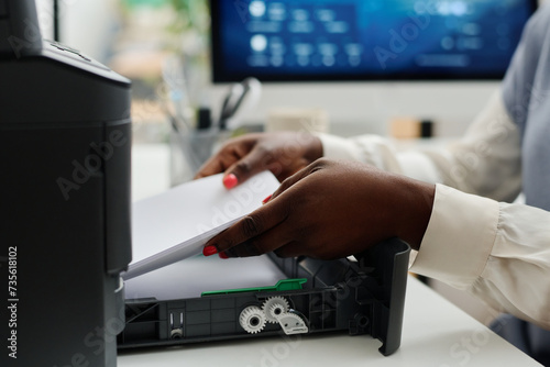 Medium closeup of hands of unrecognizable African American female office worker filling printer tray with sheets of paper photo