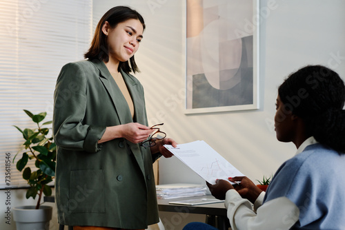 Young female manager wearing stylish smart casual clothes handing in document to her colleague photo