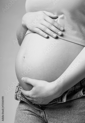 Black and white photo of young female touching with hands her naked belly. Baby expectation concept.