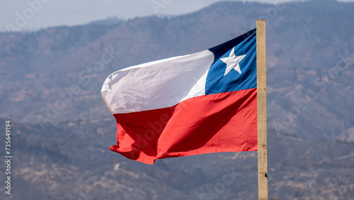 bandera chilena  en mastil de madera sin pintar, de fondo se ve un cerro o montaña desenfocado photo
