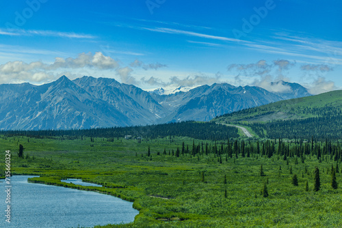 Scenic Highway in Alaska to the Alaska Range mountains on horizon at the end of long highway with green trees on side of highway. 