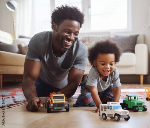A black toddler boy and his father playing with his trucks together on the floor. They are smiling and having fun.