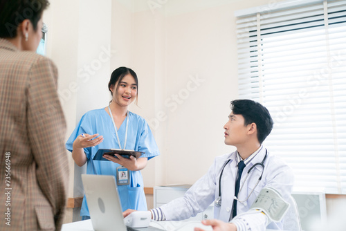Mature female doctor discussing medical report with nurses in hospital hallway. Senior general practitioner discussing patient case status with group of medical staff after surgery. Doctors working.