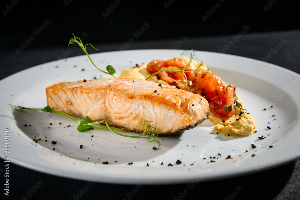 Close-up of salmon steak with hummus and tomatoes on a white plate