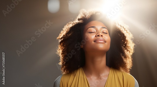 Meditation concept. Beautiful young black woman stands in meditative pose, enjoys peaceful atmosphere, holds hands in praying gesture, isolated over white background, has sense of inner peace photo