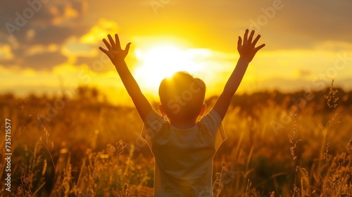 A little boy raises his hands above the sunset sky, enjoying life and nature. Happy kid on a summer field looking at the sun. Silhouette of a male child in the sun. Fresh air, environment concept photo