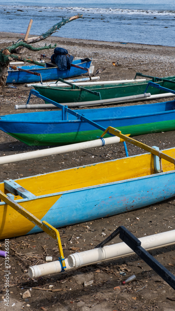 A row of colorful, traditional wooden fishing canoe boats with outrigger in bright blue and yellow on tropical island destination of Timor-Leste in Southeast Asia A row of colorful, traditional wooden fishing canoe boats with outrigger in bright blue and yellow on tropical island destination of Timor-Leste in Southeast Asia