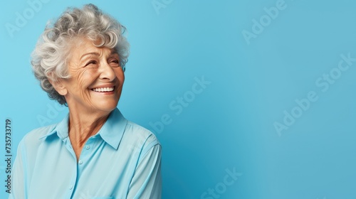 A beautiful elderly woman in an elegant shirt on an isolated blue background. The woman smiles and laughs. A place for the text.