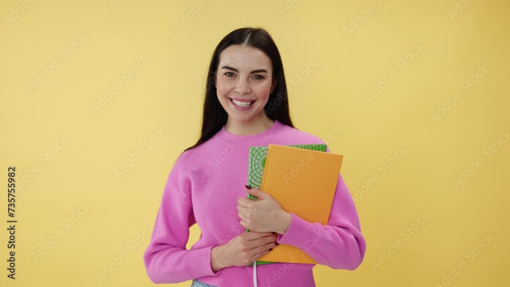 Adorable woman standing on yellow background and holding copybooks in hands. Capable university student in pink clothes feeling excited about new studying year and ready to get useful knowledge. Adorable woman standing on yellow background and holding copybooks in hands. Capable university student in pink clothes feeling excited about new studying year and ready to get useful knowledge.