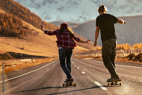 Young couple hipsters are training to ride on longboards at sunset mountain road