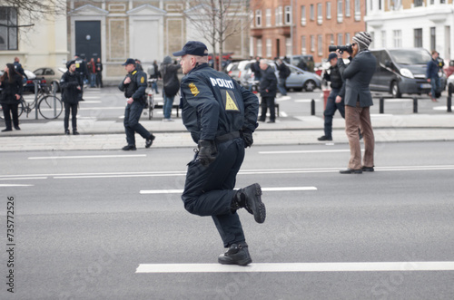 Police officer, man and running in street with crowd safety with protection service for public in city. People, law enforcement and justice in danger, arrest or warning on urban road in Copenhagen