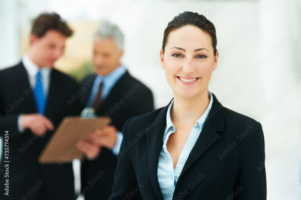 Woman, portrait and colleagues in background of office with smile for business of corporate company. Person, happy and professional as employee with suit and collaboration with team to work for job Woman, portrait and colleagues in background of office with smile for business of corporate company. Person, happy and professional as employee with suit and collaboration with team to work for job