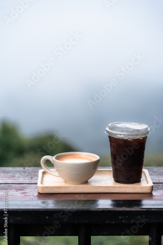 Americano iced coffee or black coffee and Hot milk tea in cup on wood desk with Foggy forest Beautiful landscape Scenic view of misty mountain nature background.