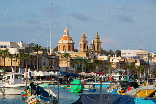 View of colorful fishing boats in Marsaxlokk harbor with the Parish Church of Our Lady of Pompei in the background, Malta