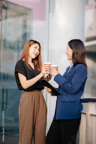 Businesswoman and woman going in city center in smart casual business style, talking, working together, stylish freelance people, holding coffee