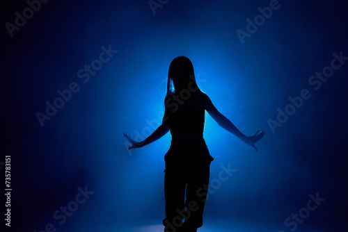 Silhouette of sexy woman dancing with blue lamps in background, smoky space. She looks seductively, active and flexible. Modern contemporary dance choreography. art, style, motion concept