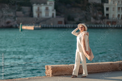 Happy blonde woman in a white suit and hat posing at the camera against the backdrop of the sea © svetograph