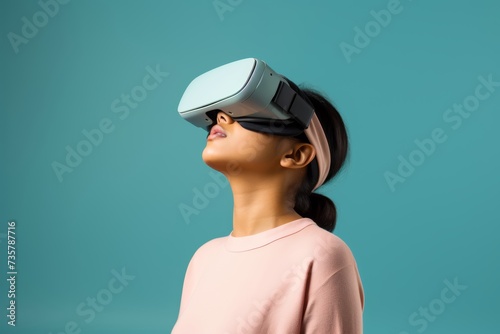 30-year-old Asian woman engrossed in virtual reality with wireless VR goggles against a soft pastel background with ample copy space, her expression conveying a sense of discovery. © Hanna Haradzetska
