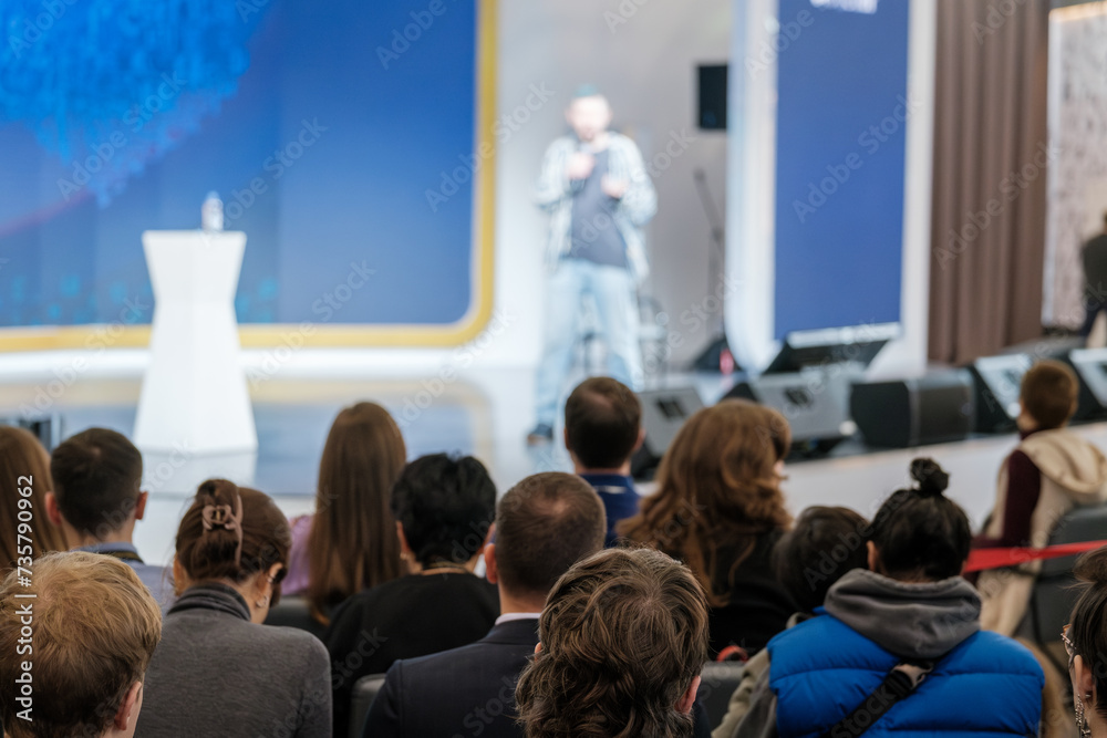 Obraz premium Focused audience at a business event listening to a speaker blurred in the background, conveying learning and engagement.