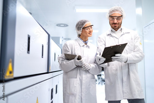 Pharmaceutical workers cooperating while working on production line machine in a medicine factory.