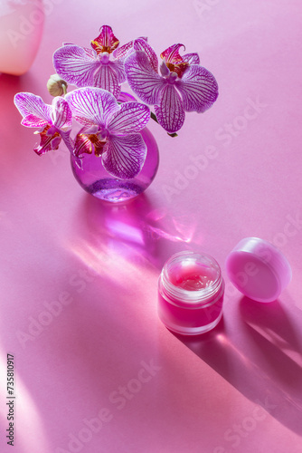 lip balm with orchid in glass vase on pink background