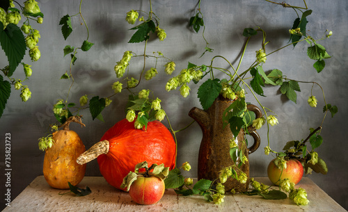 Still life with branches of climbing hops, pumpkins and ripe apples with leaves.