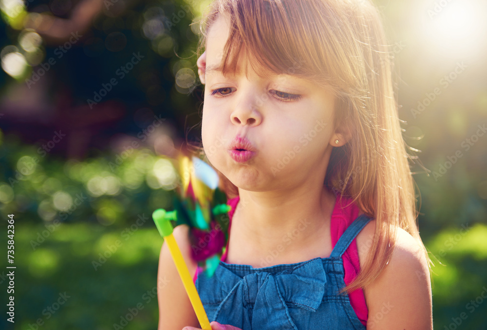 Young girl, backyard and blowing pinwheel, garden and enjoying freedom of outside and fun. Pretty little child, outdoor and summer for playing, toy and windmill for holidays and nature sunshine