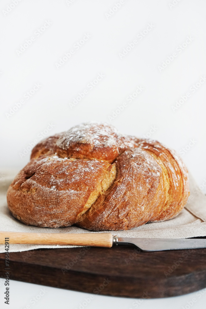 Fresh bread on a wooden board and linen tablecloth next to a knife on a white background