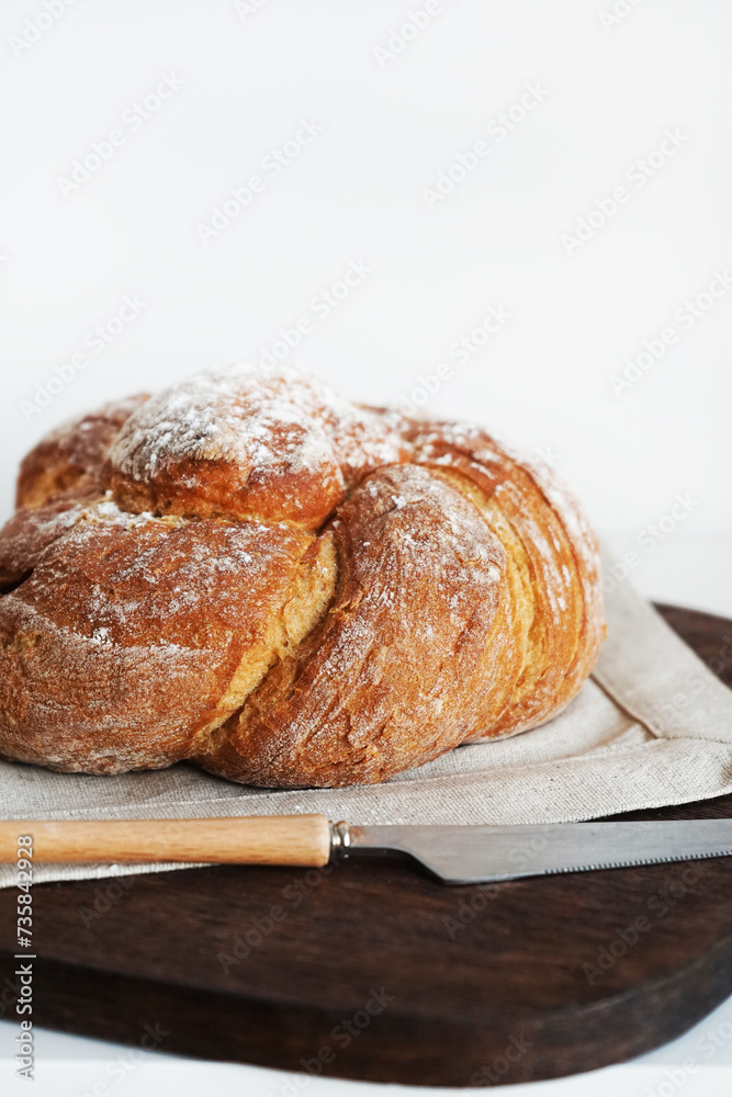Fresh bread on a wooden board and linen tablecloth next to a knife on a white background