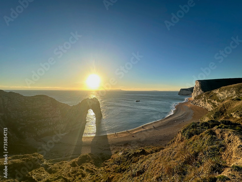 The sun goes down on the Jurassic coast and Durdle Door in Dorset with Seak Pink Trift growing on the top of the cliff in the foreground. Durdle Door, Dorset, Jurassic Coast, England, UK