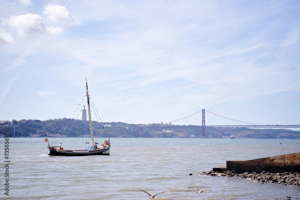 Beautiful landscape with a yacht sailing the Tejo River with the Bridge Ponte 25 de Abril view in Lisbon, Portugal