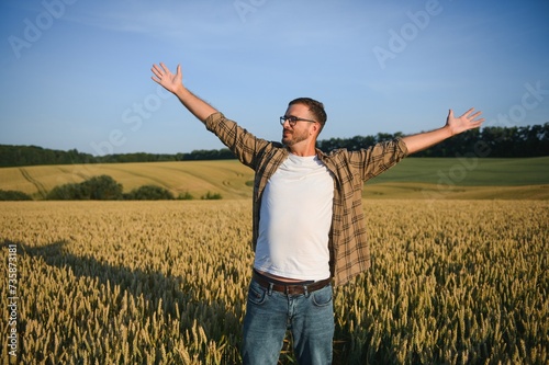 Sunny picture of happy farmer looking up in sky and outstretching hands. Stand in middle or wheat field and enjoy. Ripe harvest time. Sunrise or sunset © Serhii