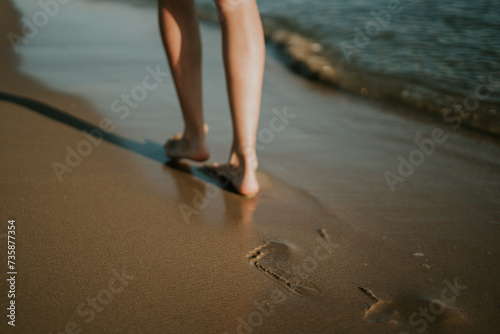 Mujer caminando por la orilla dejando sus huellas en la arena. La huella está enfocada. Puesta de sol en la playa. Date un paseo para desconectar. Ondas suaves y agradables. Hermosas piernas de mujer. photo