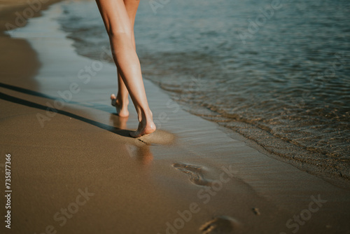 Mujer caminando por la orilla dejando sus huellas en la arena. Puesta de sol en la playa. Date un paseo para desconectar. Ondas suaves y agradables. Hermosas piernas de mujer. Relajación en verano. photo