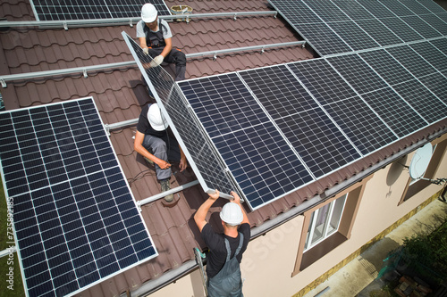 Man technician building photovoltaic solar moduls on roof of house. Mounter in helmet installing solar panel system outdoors. Concept of alternative and renewable energy. Aerial view.
