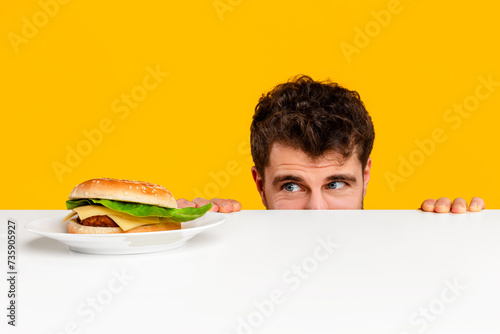 man peeking at tempting cheeseburger on plate against yellow background photo