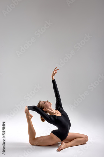 talented ambitious woman practicing yoga, sitting in Mermaid exercise, Eka Pada Rajakapotasana pose, working out, wearing black bodysuit full length, grey studio background, grace