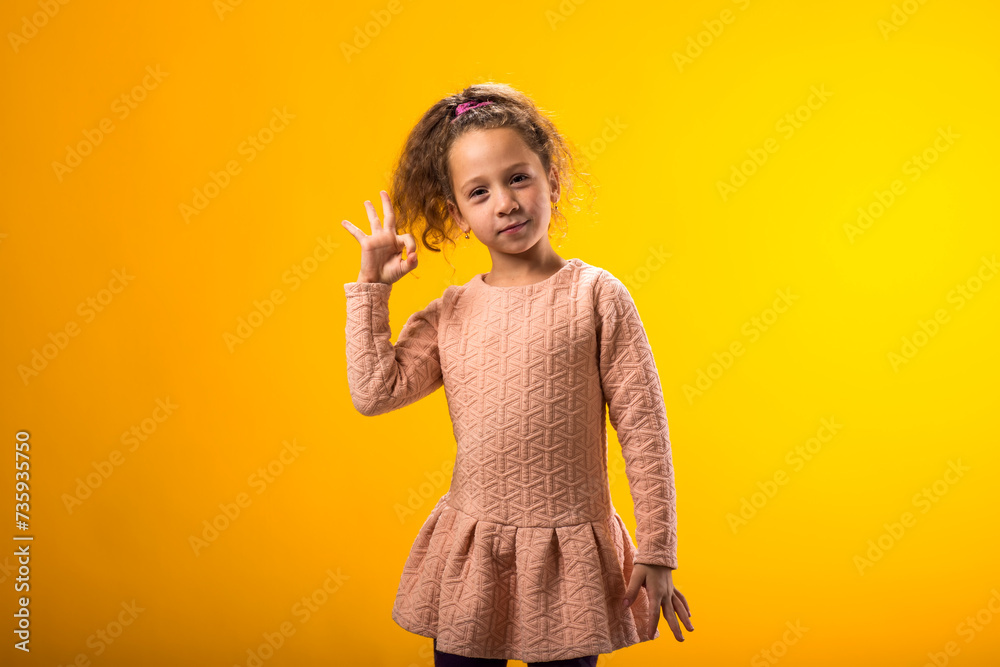 Smiling child girl showing ok gesture over yellow background. Positive emotions concept Smiling child girl showing ok gesture over yellow background. Positive emotions concept